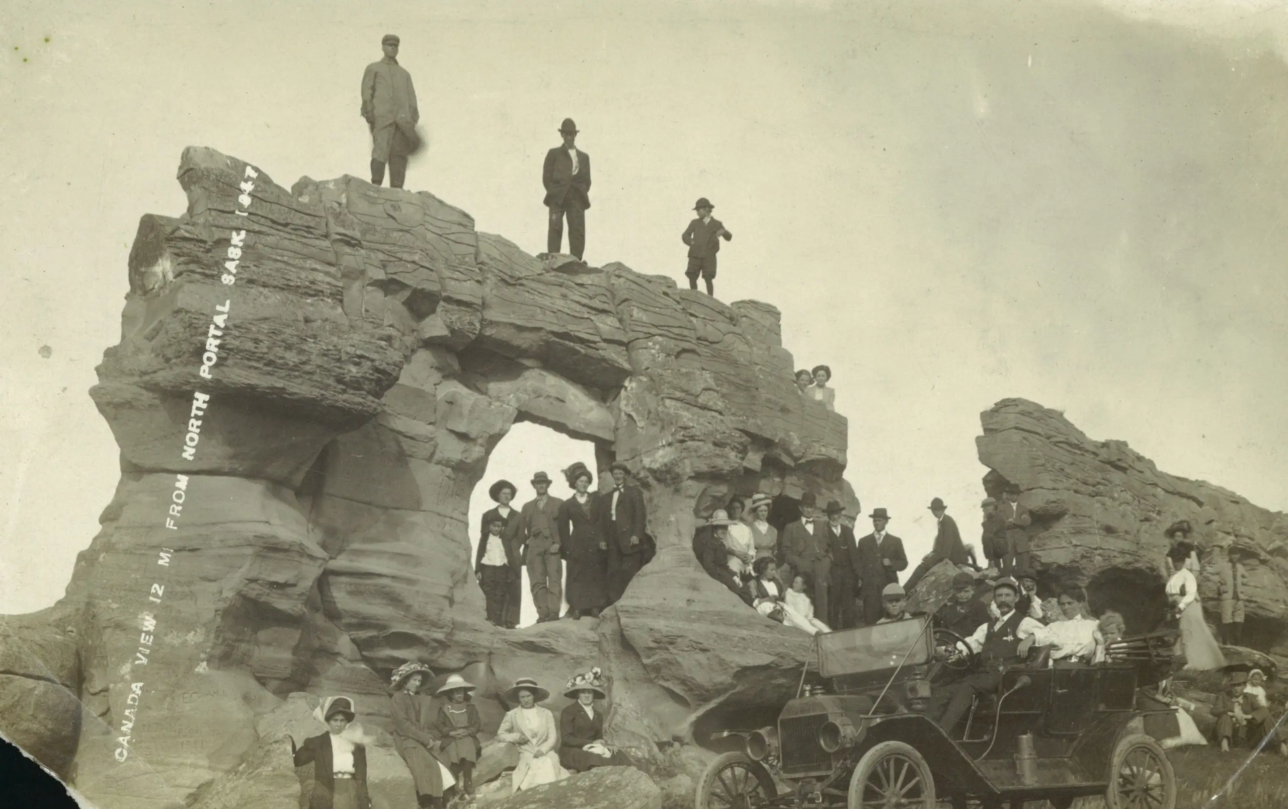 Group gathered at the rock formation with an early automobile