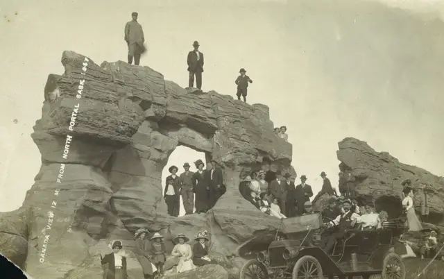 Group gathered at the rock formation with an early automobile